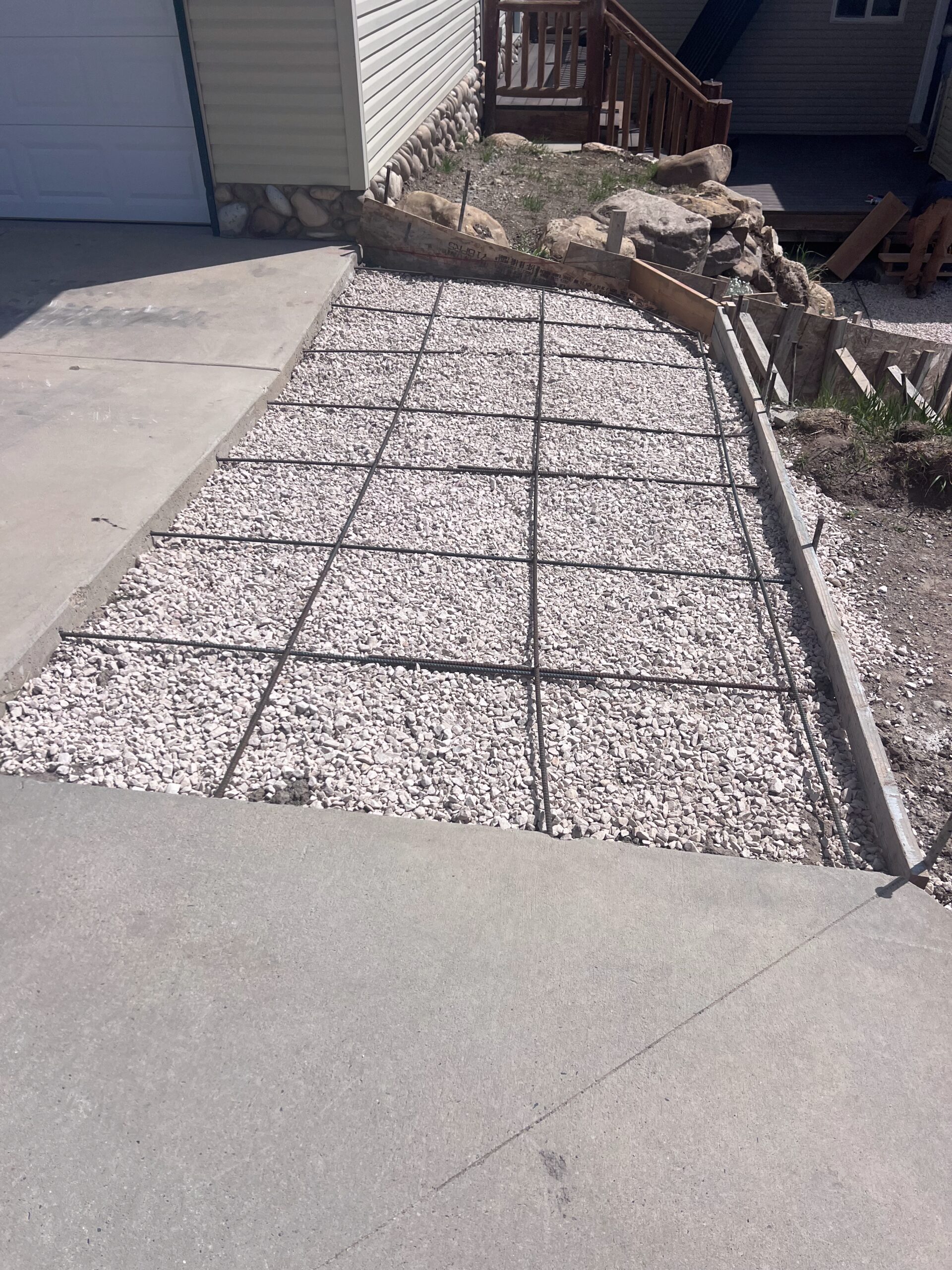 Graded gravel base with rebar grid for concrete project, showcasing preparation work by Bear Essentials Handyman Services.