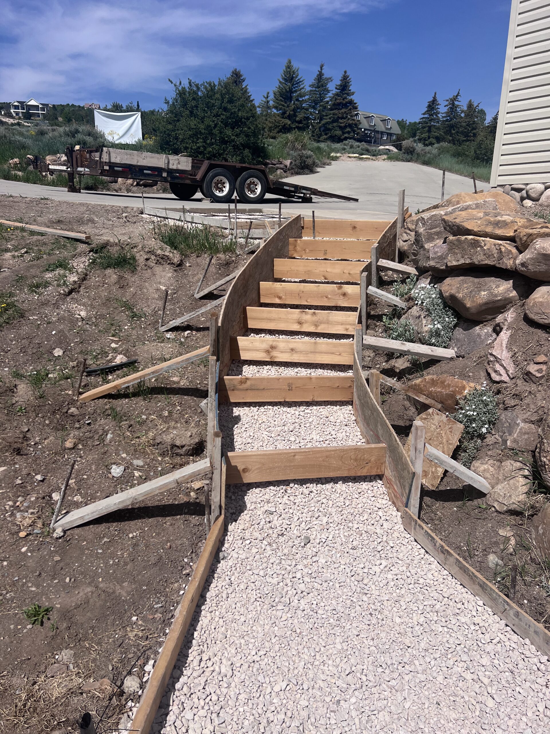 Concrete steps under construction with wooden forms and gravel, surrounded by landscaping and a trailer in the background, showcasing Bear Essentials Handyman Services' focus on quality craftsmanship and durable projects.