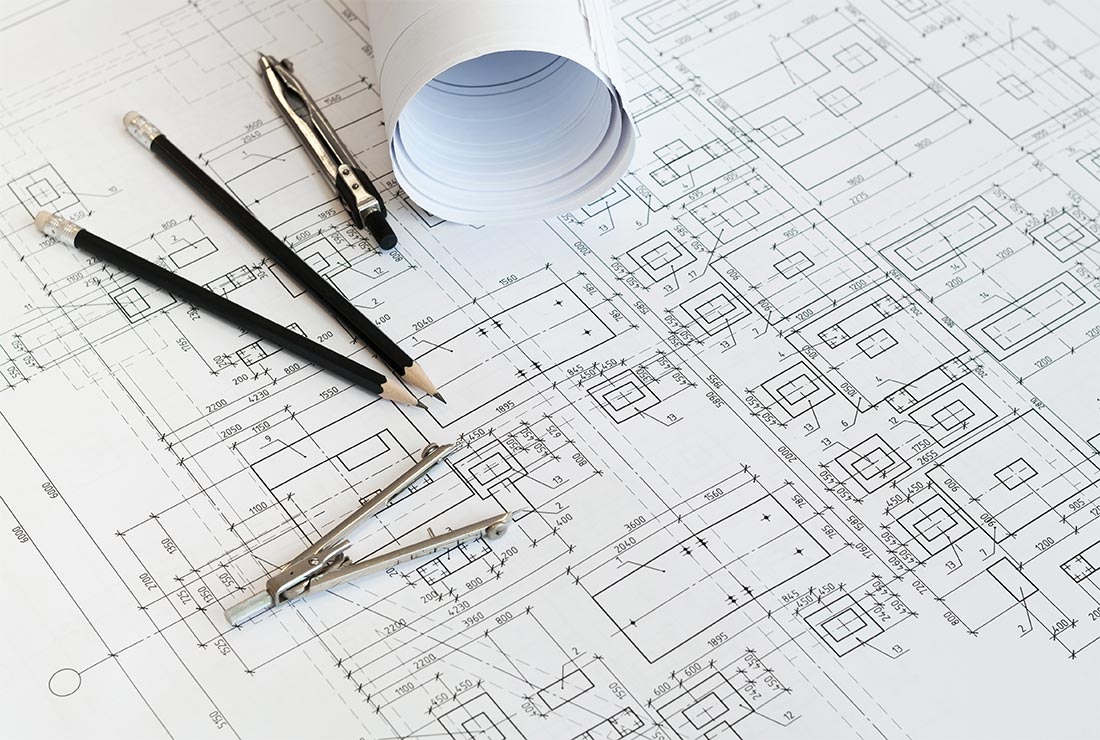 Blueprints and architectural plans with drafting tools, including pencils and a compass, on a workspace.