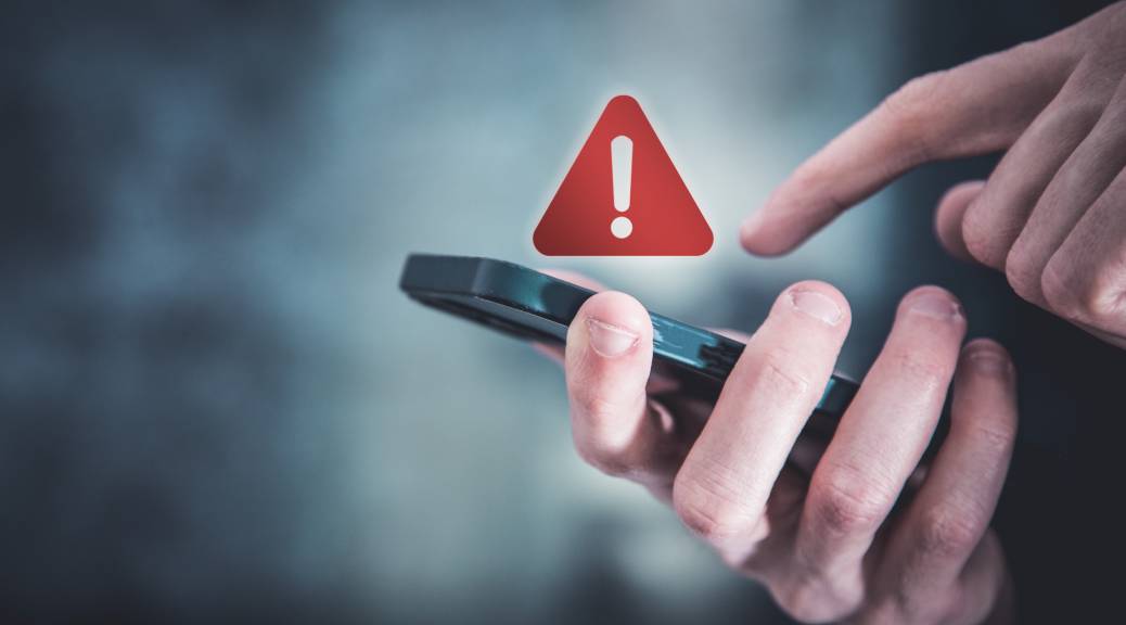 Person interacting with smartphone displaying emergency alert symbol, emphasizing the importance of emergency contact services for short-term rental compliance.
