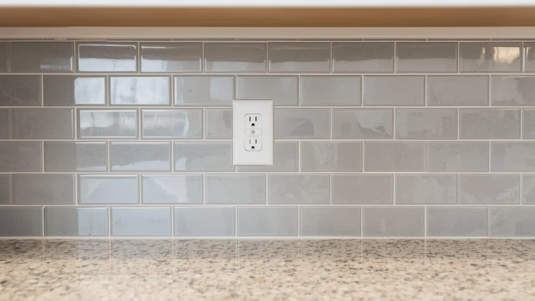 Electrical outlet on gray tiled backsplash above speckled countertop, illustrating essential electrical planning for kitchen remodels in Bloomington.