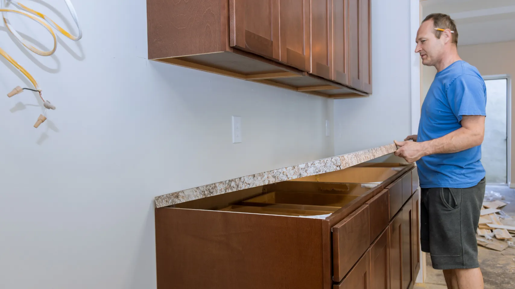 Man installing a custom countertop in a kitchen remodel, with wooden cabinets and visible electrical wiring, emphasizing proper sequencing in Bear Lake projects.